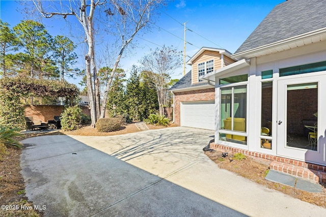 exterior space featuring a shingled roof, concrete driveway, and brick siding