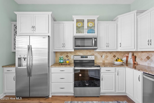 kitchen with stainless steel appliances, backsplash, light stone countertops, and white cabinets