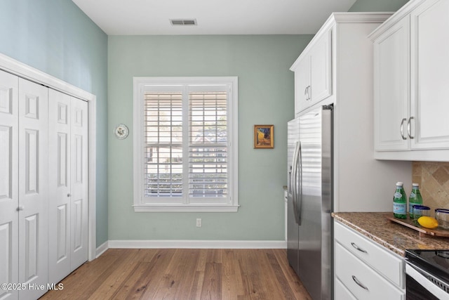 kitchen with dark wood-style flooring, visible vents, baseboards, white cabinets, and stainless steel fridge