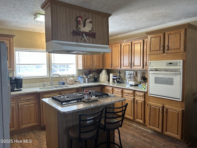 kitchen with brown cabinets, a sink, oven, and under cabinet range hood