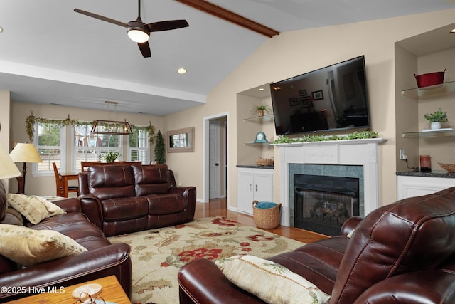 living area featuring lofted ceiling with beams, built in shelves, wood finished floors, a ceiling fan, and a tiled fireplace