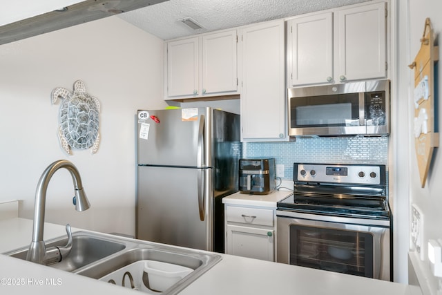 kitchen with stainless steel appliances, a sink, white cabinetry, light countertops, and backsplash