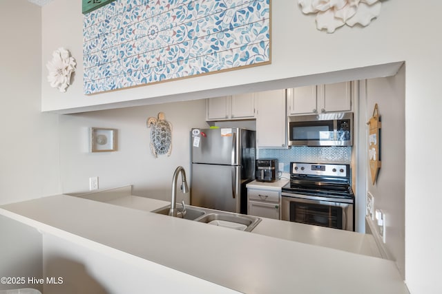 kitchen with a peninsula, a sink, light countertops, appliances with stainless steel finishes, and tasteful backsplash