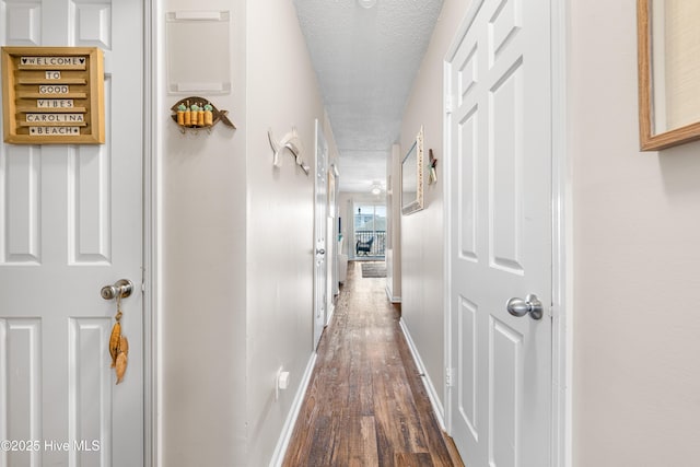 corridor with dark wood-type flooring, a textured ceiling, and baseboards