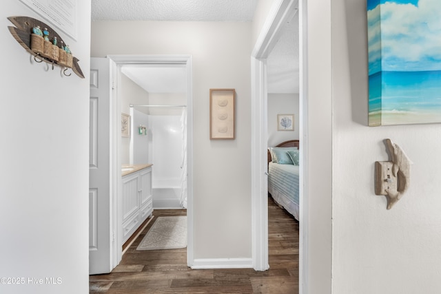 hall featuring dark wood-style flooring, a textured ceiling, and baseboards