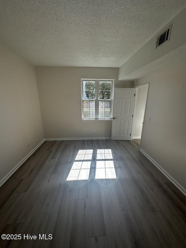 spare room with a textured ceiling, visible vents, and dark wood-type flooring