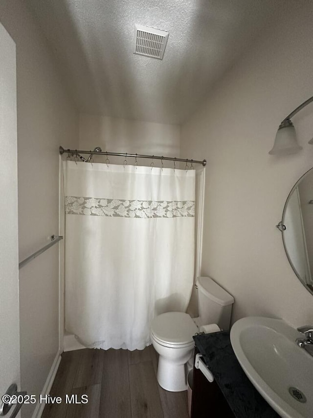 full bathroom featuring a textured ceiling, a shower with shower curtain, wood finished floors, a sink, and visible vents