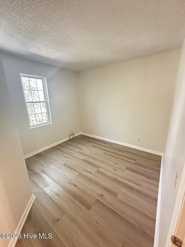 empty room featuring a textured ceiling, baseboards, and wood finished floors