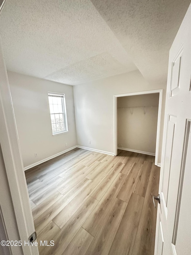 unfurnished bedroom with a textured ceiling, a closet, wood finished floors, and baseboards