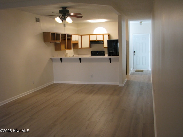 kitchen featuring visible vents, stove, light wood-style floors, under cabinet range hood, and baseboards