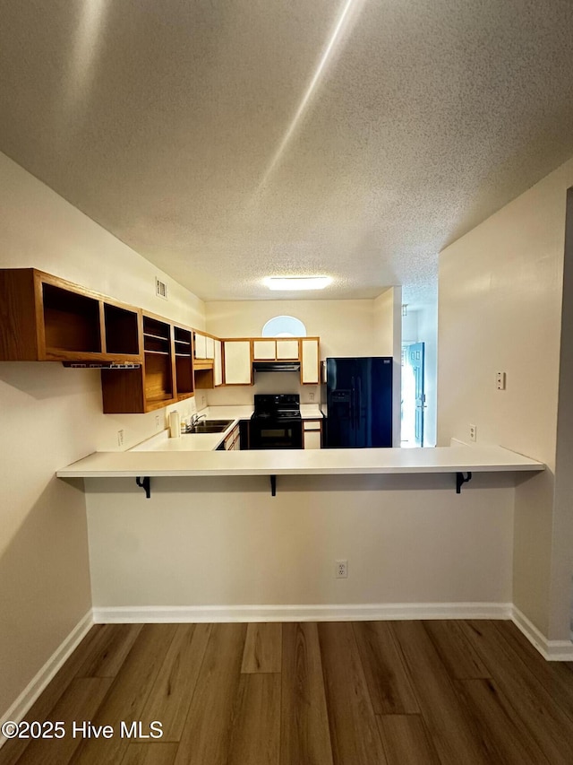 kitchen with a breakfast bar, dark wood finished floors, a peninsula, and black appliances