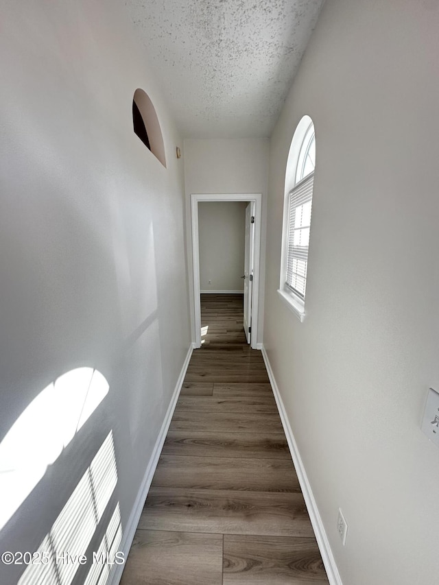 corridor with a textured ceiling, baseboards, and wood finished floors