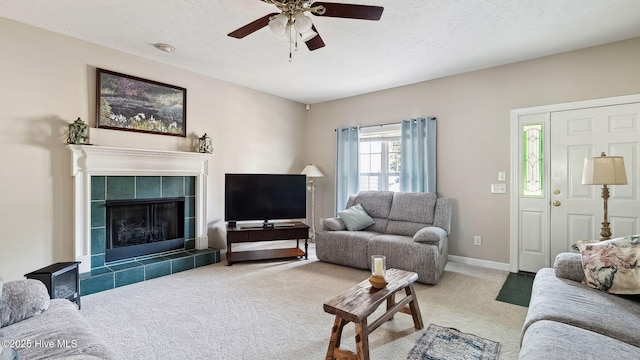 living area featuring a textured ceiling, a ceiling fan, a tiled fireplace, and carpet flooring