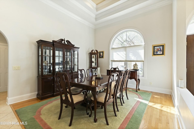 dining room featuring light wood-type flooring, arched walkways, ornamental molding, and a towering ceiling