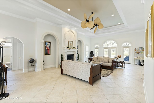 living room featuring crown molding, a fireplace, light tile patterned floors, a raised ceiling, and ceiling fan