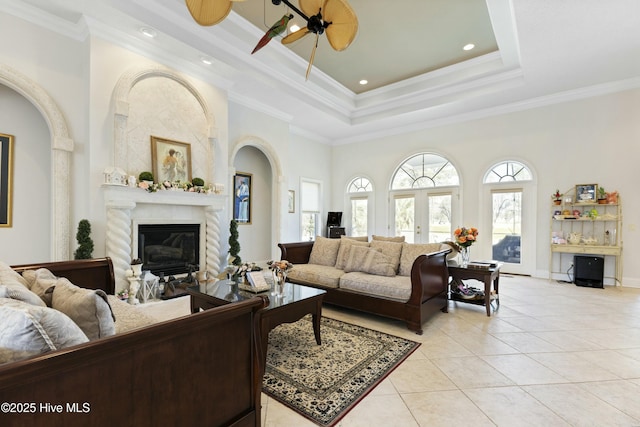 living area with light tile patterned flooring, a ceiling fan, ornamental molding, a tray ceiling, and a glass covered fireplace