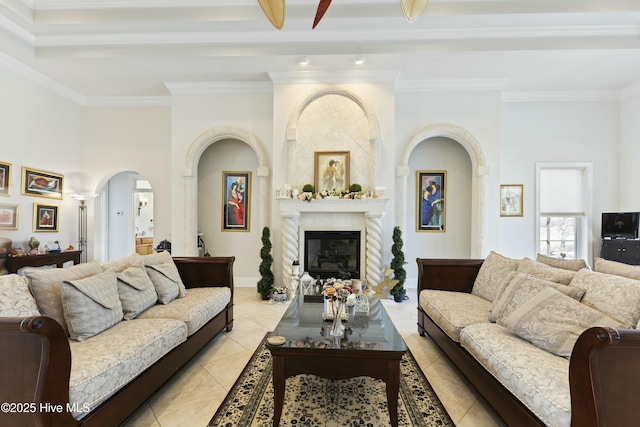 living room with ornamental molding, a glass covered fireplace, arched walkways, and light tile patterned floors