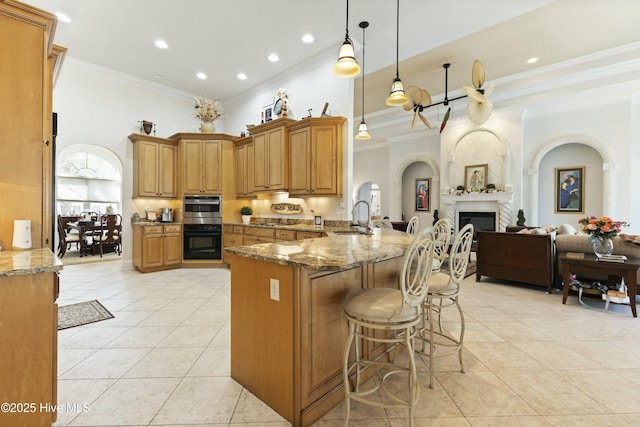 kitchen with light tile patterned floors, a peninsula, a fireplace, dark stone counters, and a kitchen bar