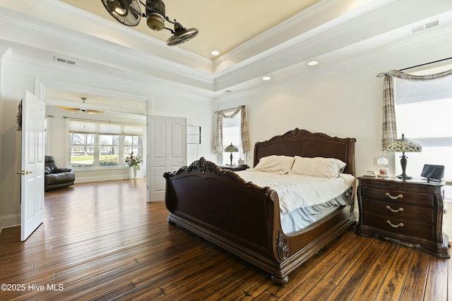 bedroom featuring ornamental molding, a tray ceiling, dark wood-style flooring, and visible vents