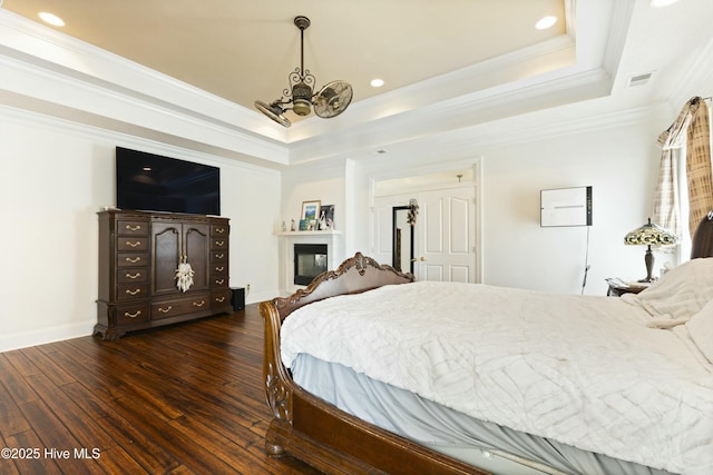 bedroom featuring dark wood finished floors, visible vents, a tray ceiling, a glass covered fireplace, and an inviting chandelier