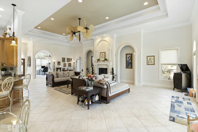 living room featuring a tray ceiling, crown molding, a fireplace, light tile patterned floors, and baseboards