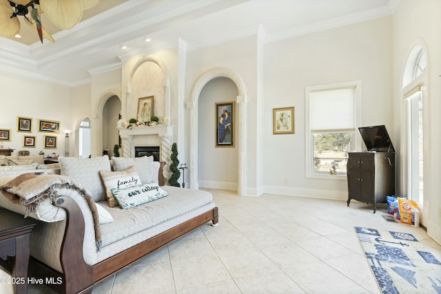 living area with light tile patterned flooring, a fireplace, a ceiling fan, baseboards, and crown molding