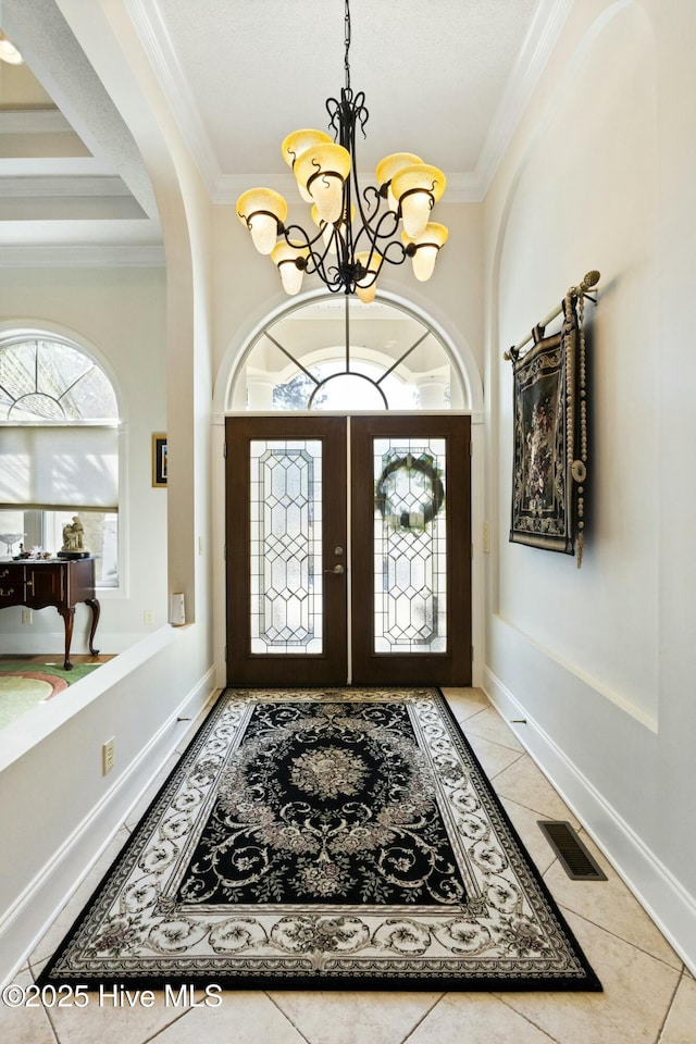 foyer entrance featuring baseboards, visible vents, an inviting chandelier, crown molding, and light tile patterned flooring