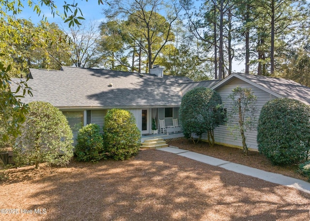 view of front of property featuring covered porch, a chimney, and a shingled roof