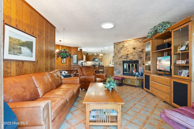 living area featuring a textured ceiling, light floors, a brick fireplace, and wooden walls