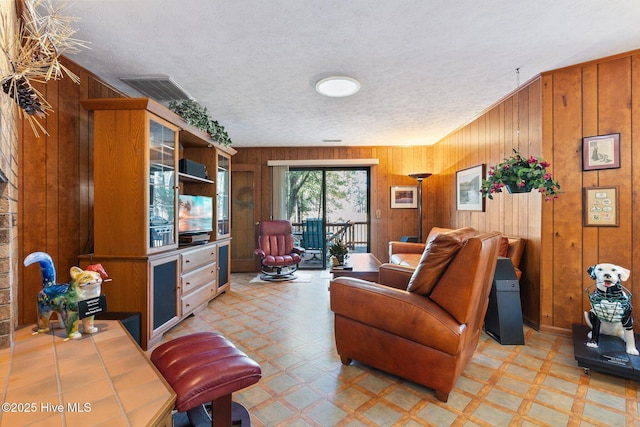 living area featuring light floors, wooden walls, visible vents, and a textured ceiling