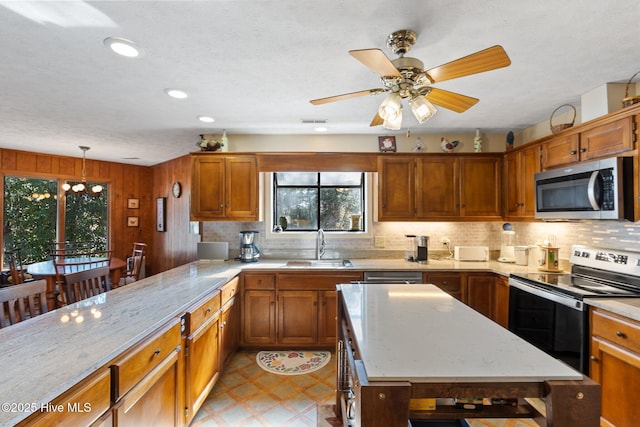 kitchen with a sink, appliances with stainless steel finishes, light floors, brown cabinetry, and pendant lighting