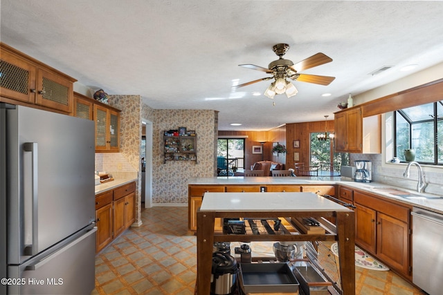 kitchen with stainless steel appliances, a sink, light countertops, brown cabinetry, and glass insert cabinets