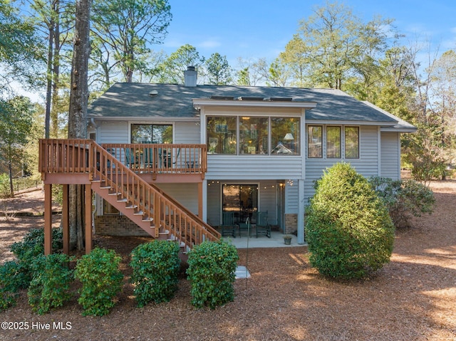 rear view of house with a patio, a chimney, a sunroom, a wooden deck, and stairs