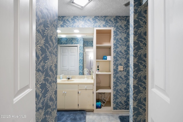 bathroom with wallpapered walls, visible vents, a textured ceiling, and vanity