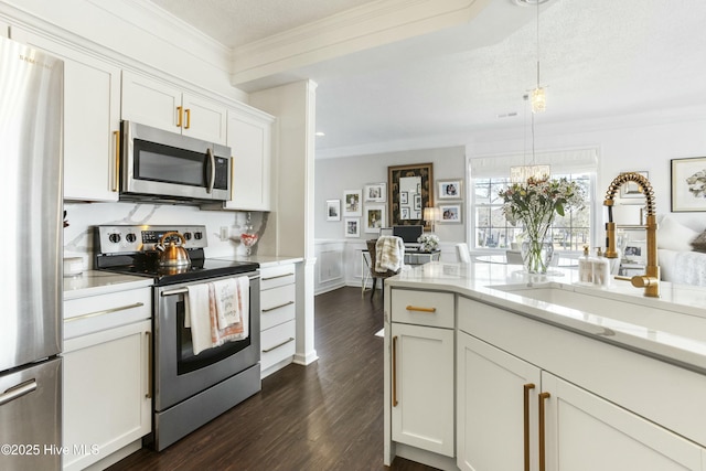 kitchen with dark wood finished floors, crown molding, stainless steel appliances, white cabinetry, and a sink