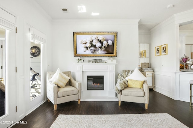 living area with crown molding, visible vents, dark wood-style flooring, and a glass covered fireplace