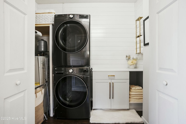 laundry room with stacked washer and dryer, water heater, and cabinet space