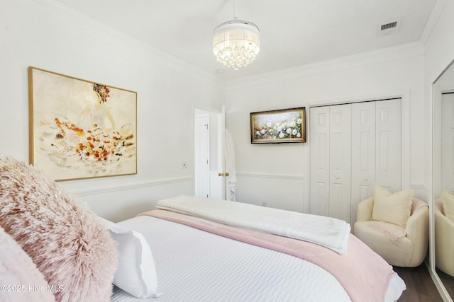 bedroom featuring visible vents, ornamental molding, wood finished floors, an inviting chandelier, and a closet