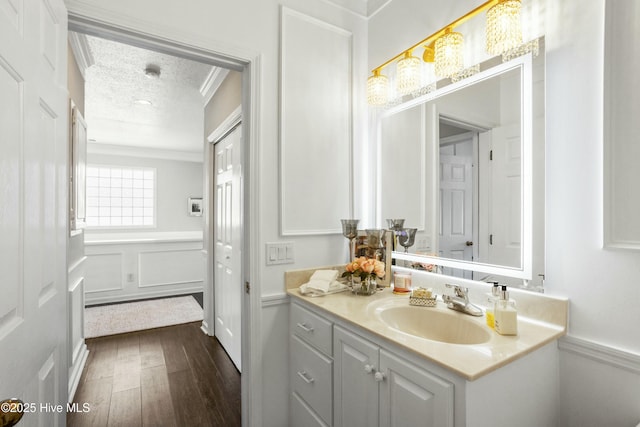 bathroom featuring a decorative wall, ornamental molding, a textured ceiling, vanity, and wood finished floors