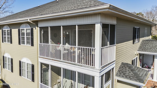 view of side of home featuring a shingled roof and a sunroom