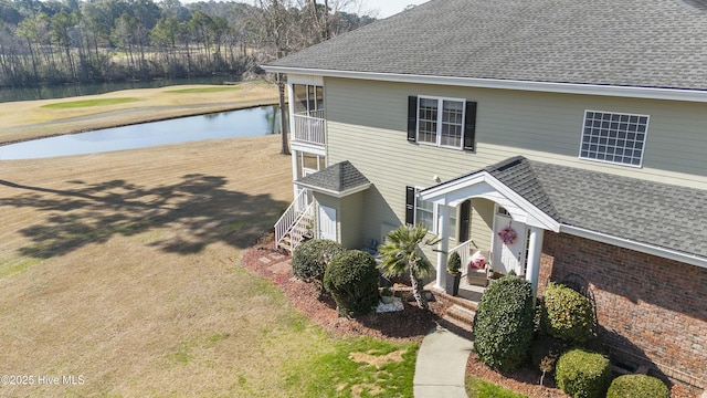 view of front of home with a water view, a shingled roof, a front lawn, and brick siding