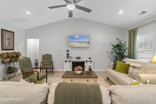 living area with vaulted ceiling, visible vents, a fireplace, and light wood finished floors