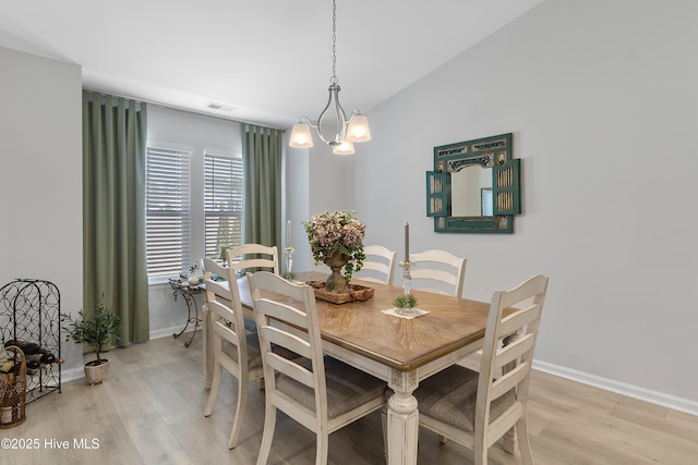 dining space with light wood-style flooring, visible vents, baseboards, vaulted ceiling, and an inviting chandelier