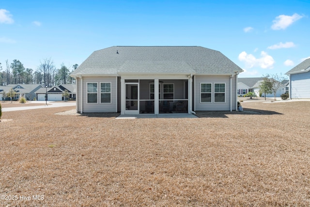 rear view of property featuring a shingled roof, a lawn, and a sunroom