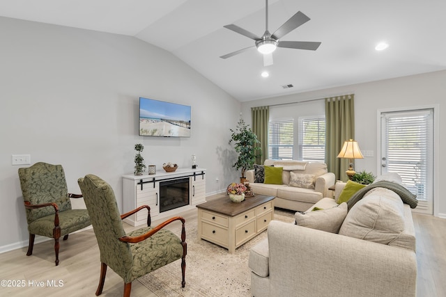 living room featuring lofted ceiling, light wood-style flooring, a ceiling fan, baseboards, and a glass covered fireplace