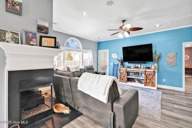 living room featuring baseboards, ceiling fan, crown molding, light wood-type flooring, and a fireplace