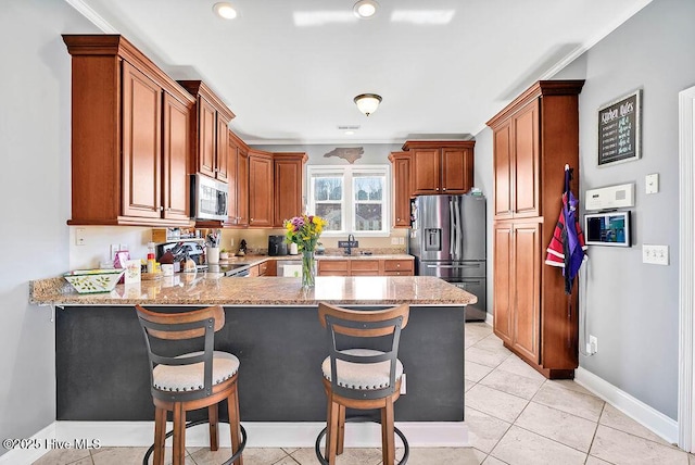 kitchen featuring appliances with stainless steel finishes, brown cabinets, light stone counters, and a kitchen breakfast bar