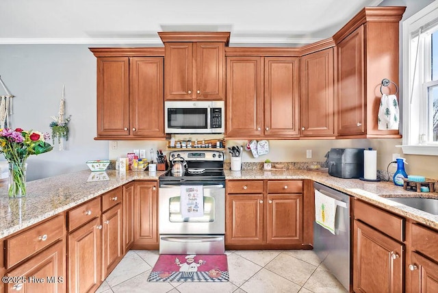 kitchen with light tile patterned floors, stainless steel appliances, light stone countertops, and brown cabinets