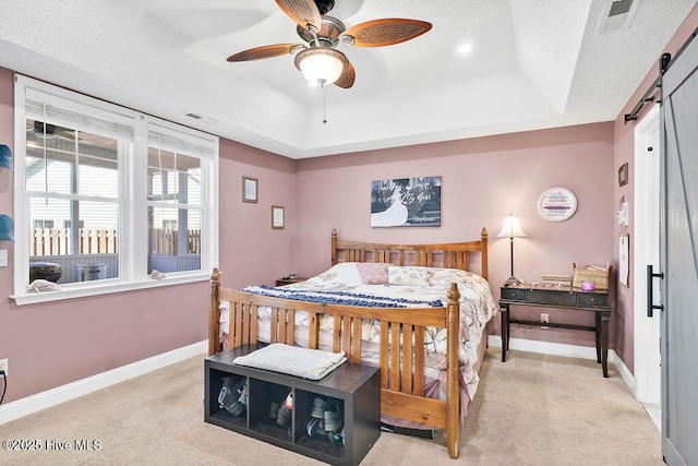 bedroom featuring a barn door, visible vents, a raised ceiling, and baseboards