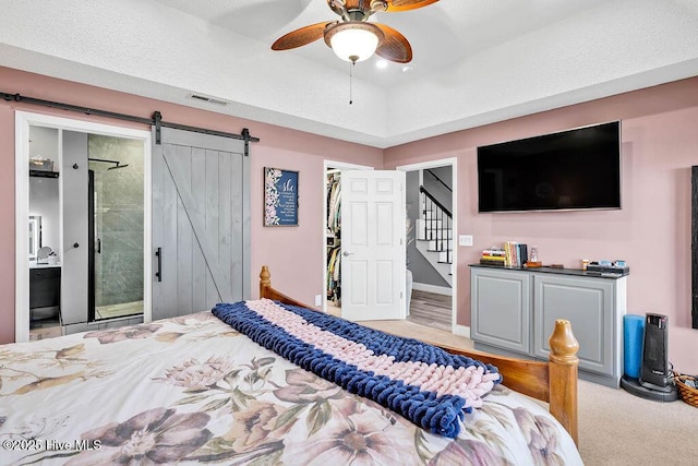 bedroom featuring a walk in closet, visible vents, a barn door, ceiling fan, and connected bathroom